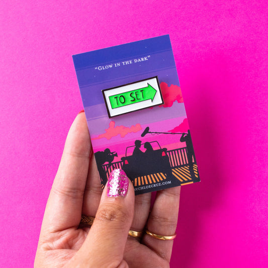 Hand holding green glow in the dark to set location arrow sign enamel pin